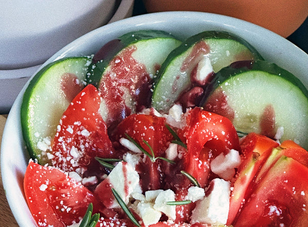 bowl of sliced cucumbers, tomato wedges, feta cheese and blueberry balsamic with a rosemary sprig garnish