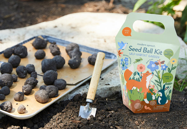 Modern Sprout Seed Ball Kit package next to a metal tray of seed balls in the yard