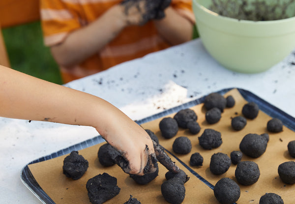 Child's hands forming seed balls on a baking sheet