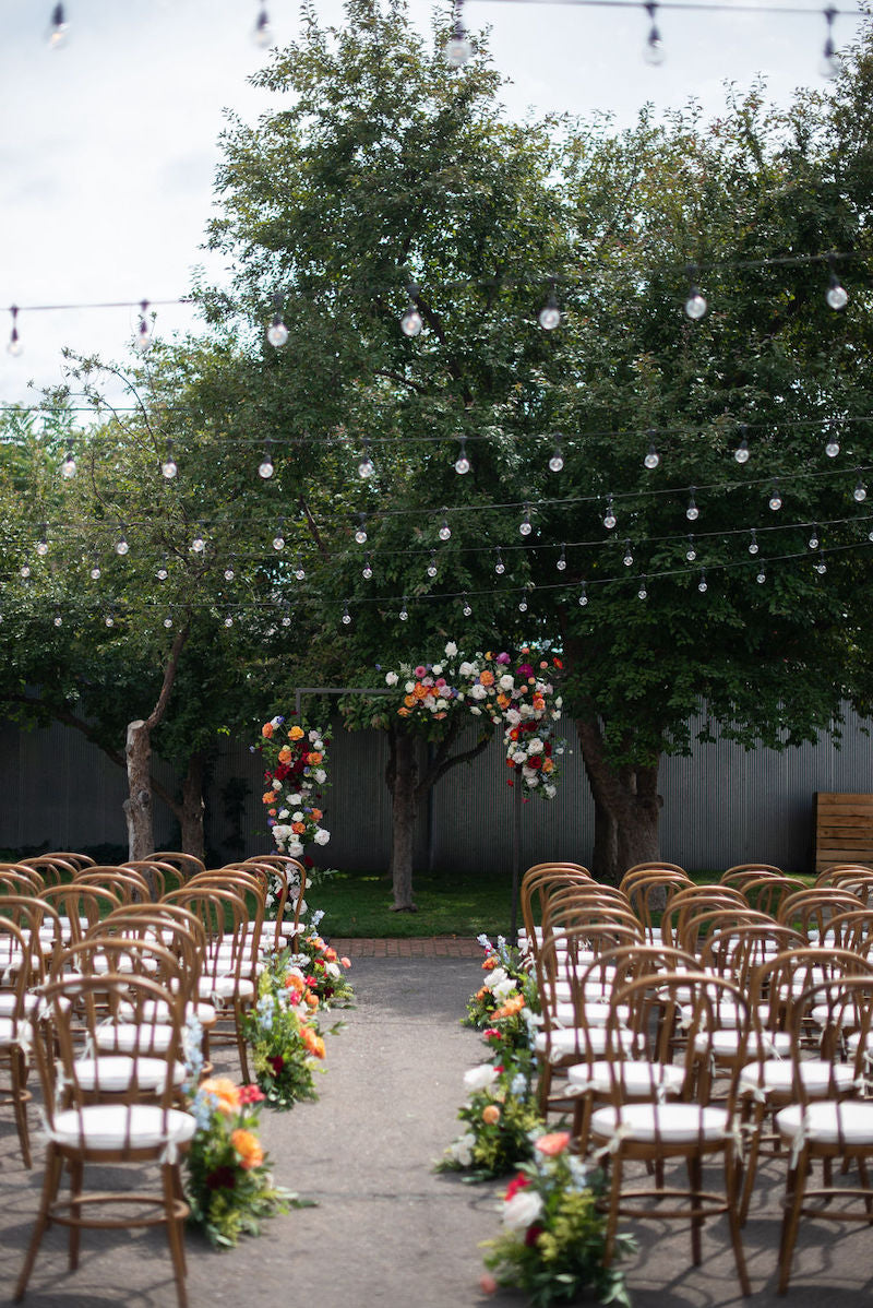 Outdoor Wedding Ceremony With Bright Colored Flowers and Hanging Lights