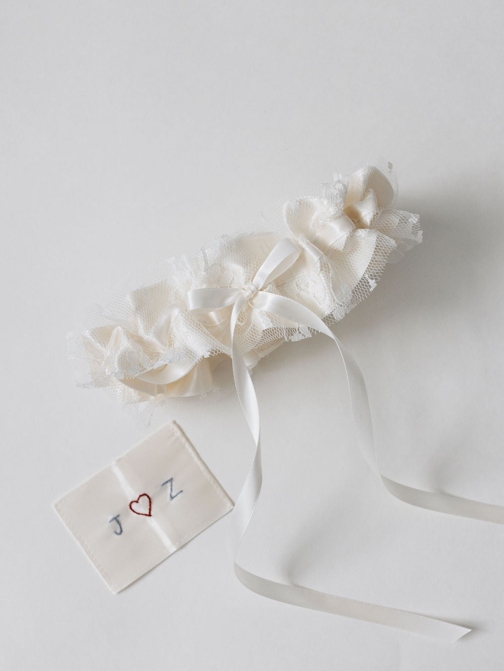 white satin wedding garter with lace overlay and hand-embroidered patch with couple's initials handmade by wedding expert The Garter Girl