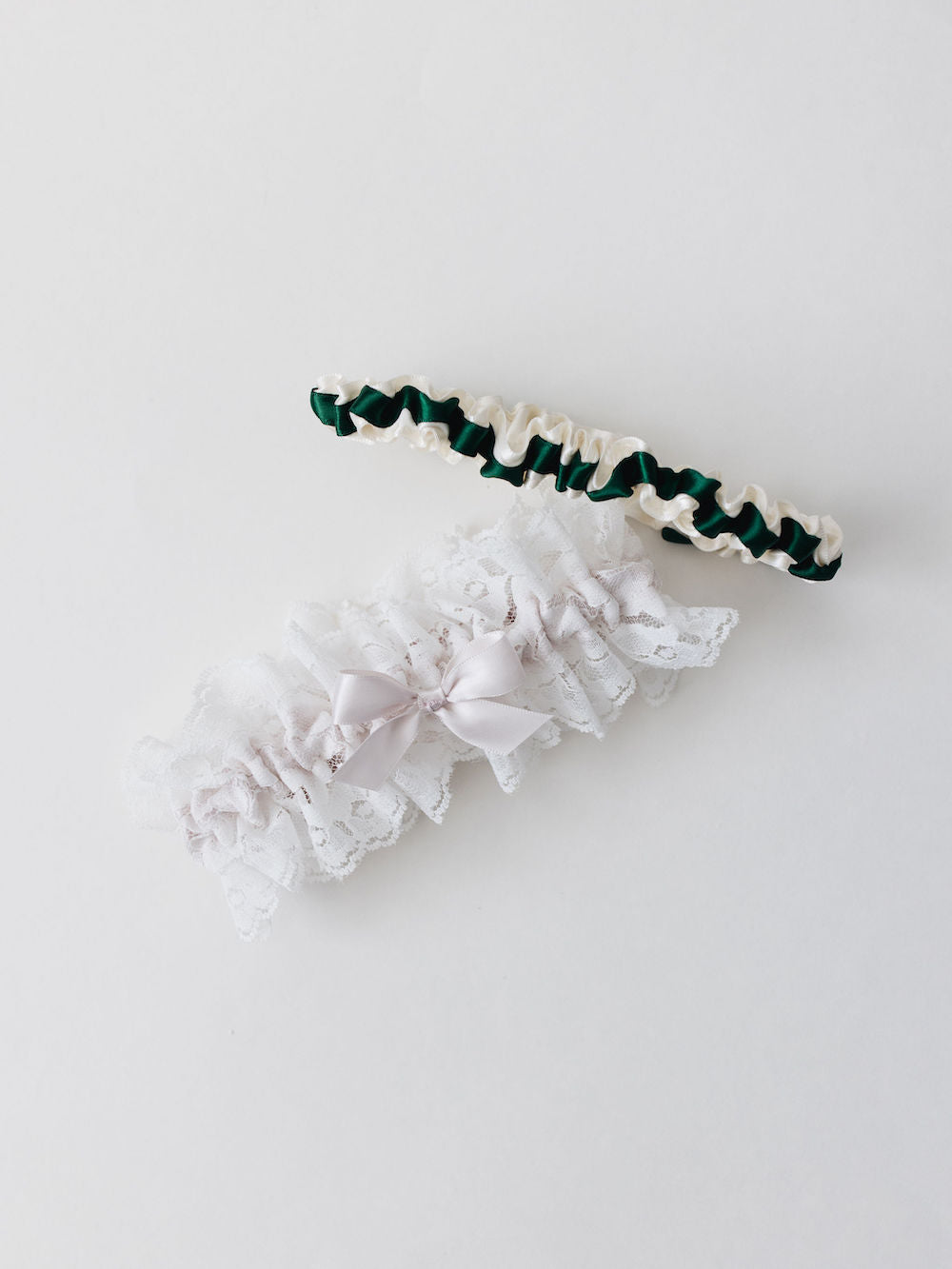 two personalized wedding garters with ivory satin and a green satin ribbon and ivory lace with a blush pink satin bow handmade by The Garter Girl