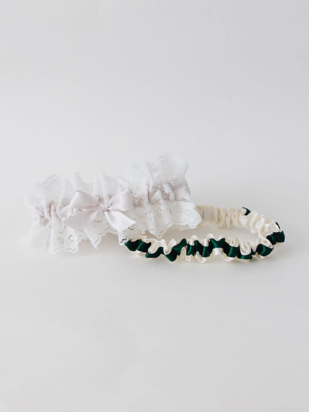 two personalized wedding garters with ivory satin and a green satin ribbon and ivory lace with a blush pink satin bow handmade by The Garter Girl