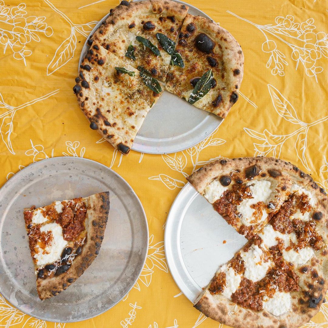 Three pizzas with one slice each on plates, on a yellow tablecloth with floral designs.
