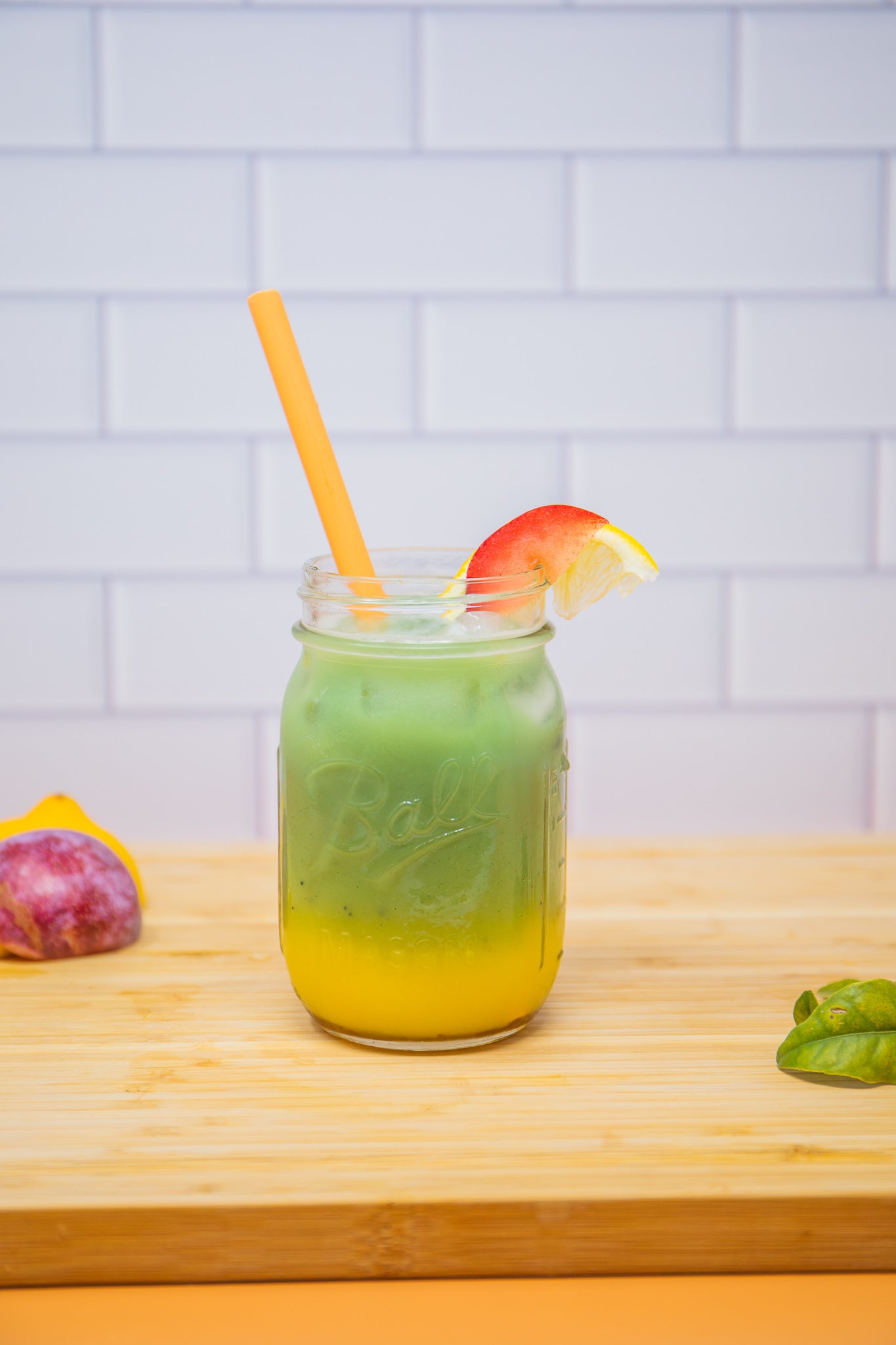 Layered green and yellow smoothie in a mason jar with a straw and fruit slice.
