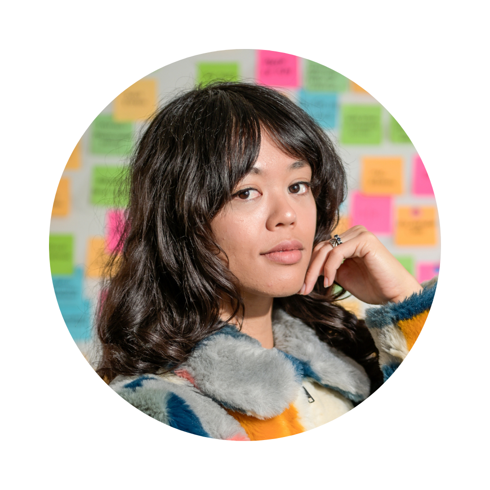 Woman with colorful fur jacket in front of post-it note wall.