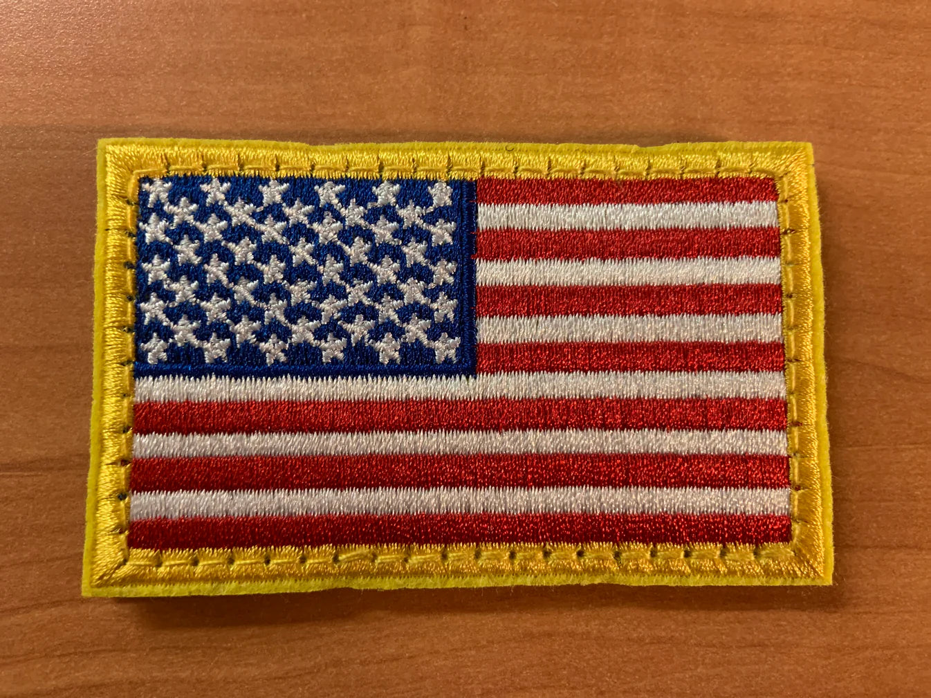Embroidered American flag patch with gold border displayed on a wood surface—compact patriotic gift for tactical dads who wear their pride daily.