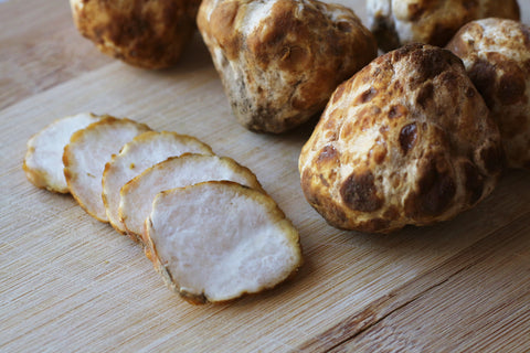 Five white and golden rimmed slices stacked on top of each other, placed on a wooden board on the left. On the right are five golden, brown-spotted, lumpy balls