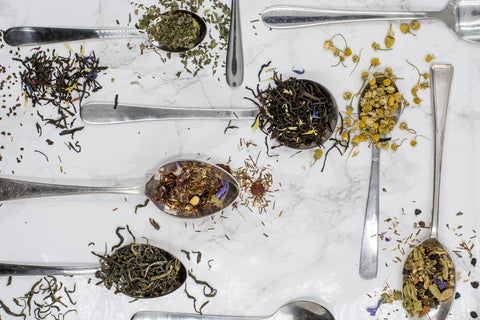 Several "deliteacious" teas and tisanes with herbs and spices on spoons.