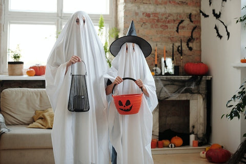 two kids dressed up as ghosts holding Halloween basket