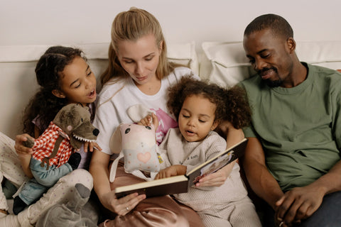 A family of four on a couch while the mother is reading aloud to her children.