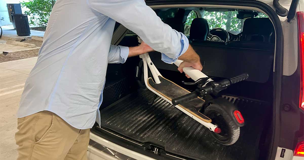 A person placing an electric scooter into the trunk of a car, preparing for winter storage to protect against cold weather.