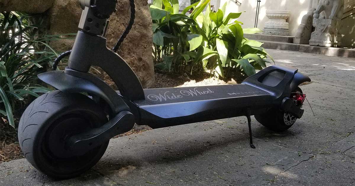 An electric scooter stands on a sidewalk with fallen leaves around, indicating the approach of winter and the need for seasonal care
