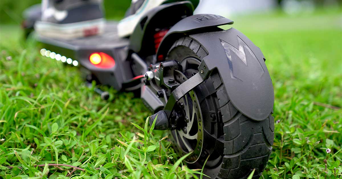 Close-up view of an electric scooter's rear wheel with a focus on the tread pattern, set against vibrant green grass, highlighting the racing modifications for the Electric Scooter Racing Series Championship.