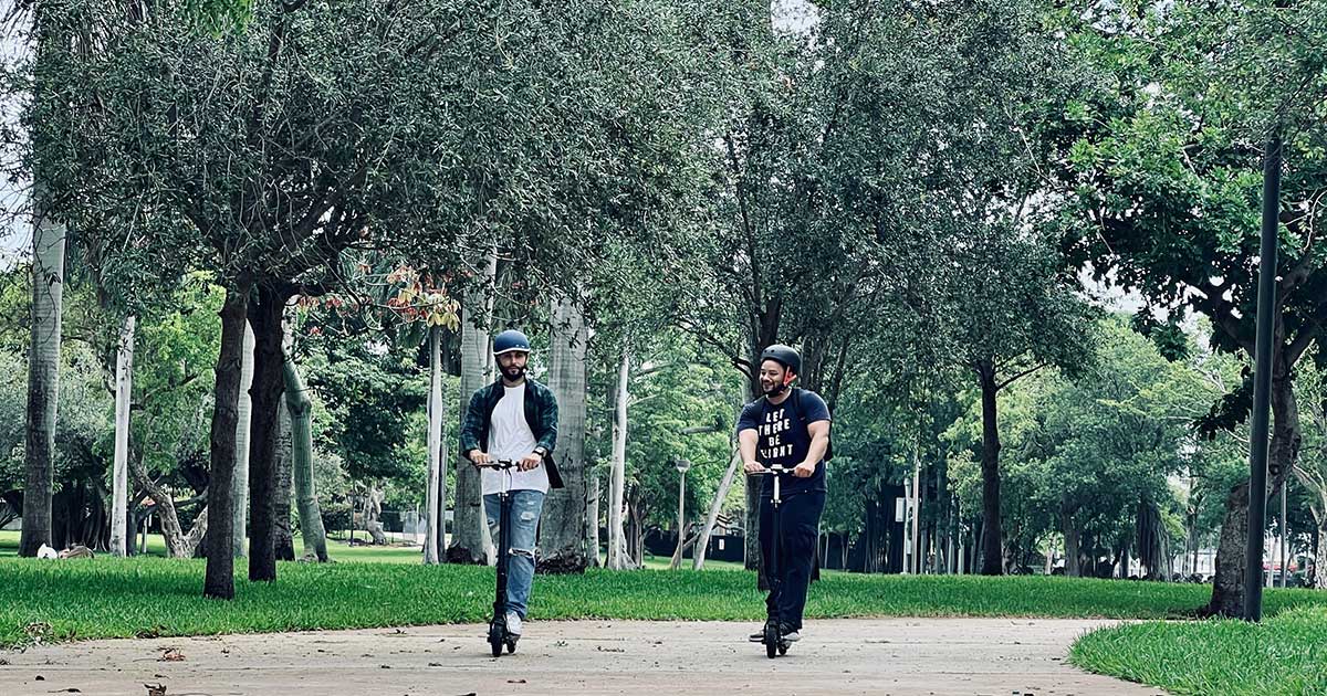Two electric scooter riders share a path in a lush park, highlighting the benefits of sensible electric scooter laws on public freedom and safety.