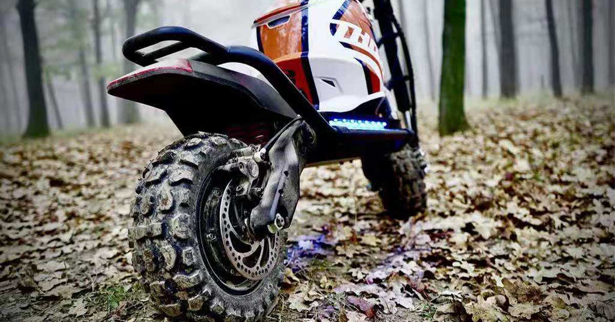 A robust electric scooter with chunky off-road tires parked in a forest, indicative of the extreme conditions faced by riders in the Electric Scooter Racing Series Championship.