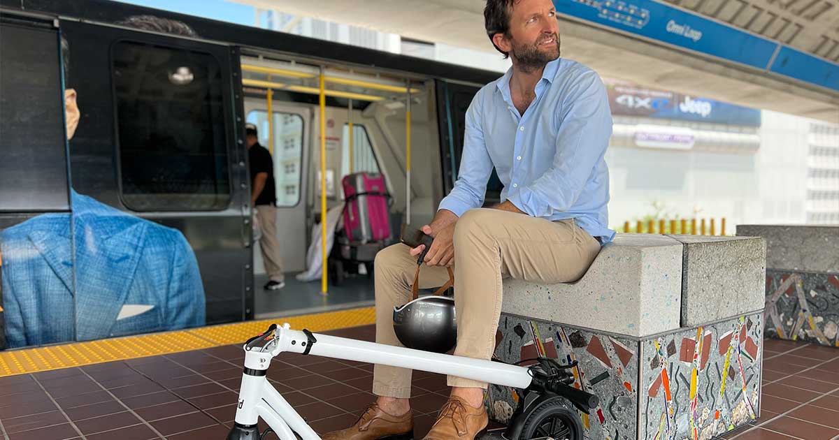 A commuter waits with a folded electric scooter at a train station, exemplifying the synergy between eco-friendly personal devices and public transit.