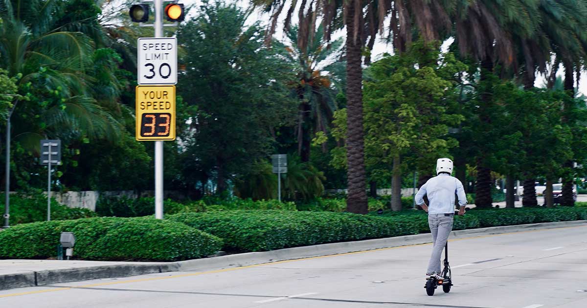 A person riding an electric scooter speeds past a speed limit sign on a city street, embodying the fusion of swift transportation and sustainability in urban environments.