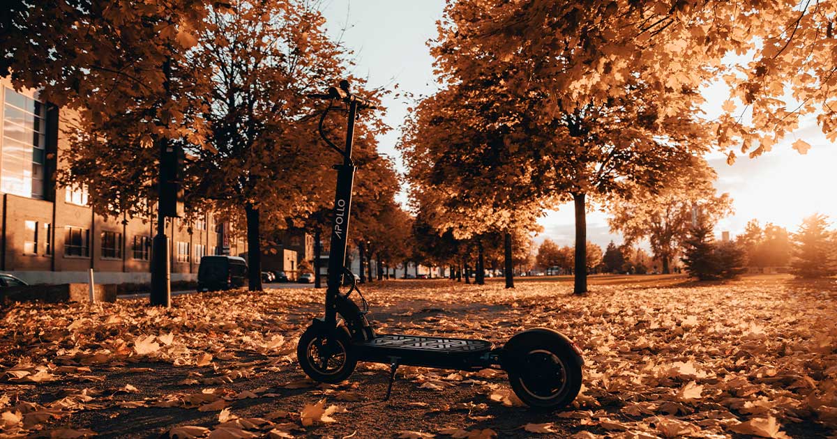 A solitary electric scooter stands in a park strewn with autumn leaves, serving as a metaphor for change and the transformation towards more climate-friendly transportation options.