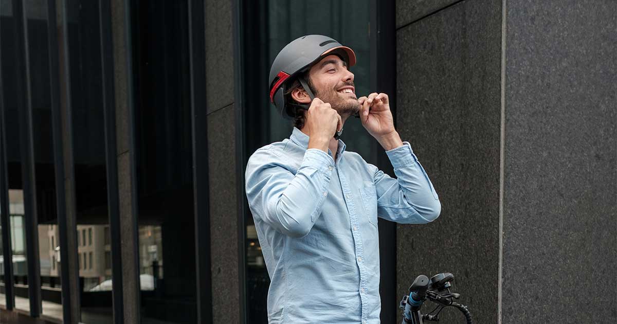 A cheerful man fastens his helmet before riding an electric scooter, highlighting the importance of safety in the growing electric scooter movement.