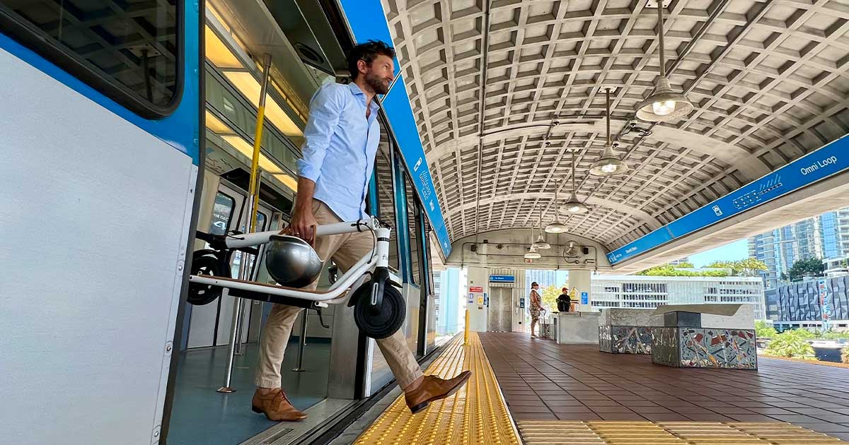 A man exits a train with an electric scooter in hand, demonstrating how electric scooters are complementing public transportation and revolutionizing urban commutes.
