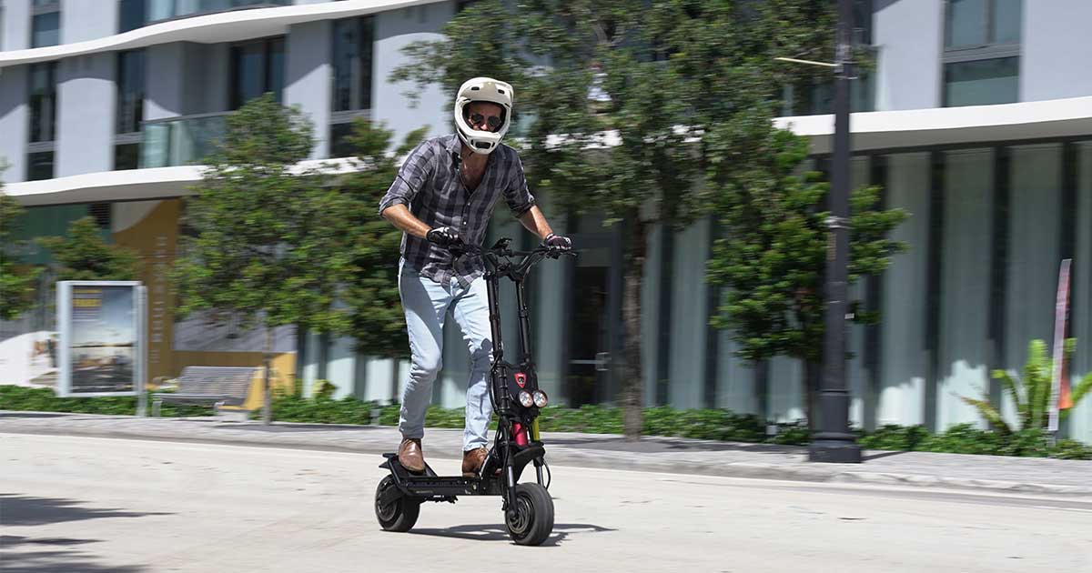 A man wearing a helmet rides an electric scooter on an urban street, illustrating the role of personal electric vehicles in promoting sustainable city living and combating climate change.