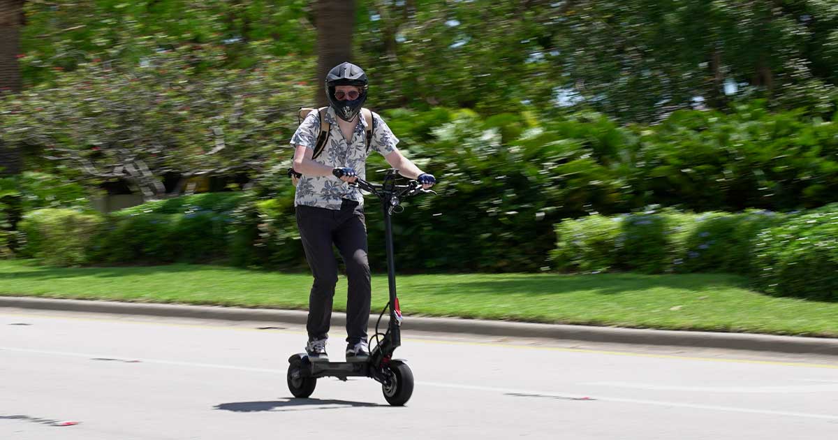 A person in casual wear enjoys a ride on a black electric scooter, navigating through a lush urban park, demonstrating the electric scooter's journey from a leisurely toy to a legitimate mode of urban transport.