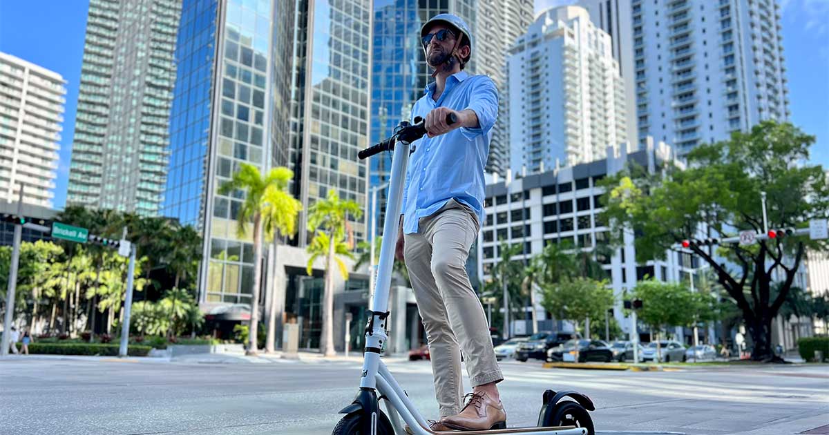 A person riding a white electric scooter across a city crosswalk, showcasing the integration of electric scooters in urban traffic and the importance of road safety.