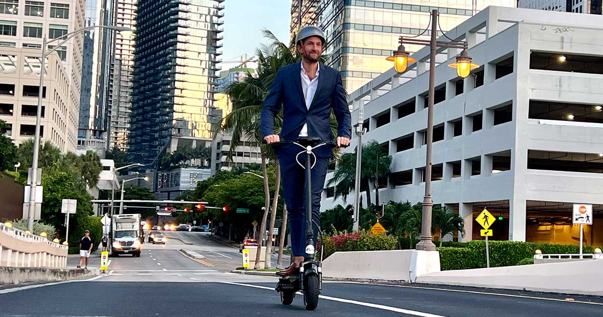 A smartly dressed individual riding an electric scooter on a city road during dusk, reflecting the importance of visibility and road safety.