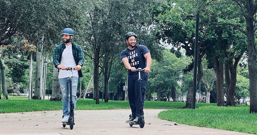 Two men enjoying a ride in the park on their own electric scooters