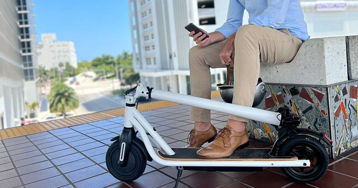 A man seated on an electric scooter checking his smartphone for the best apps for electric scooter enthusiasts in an urban setting.