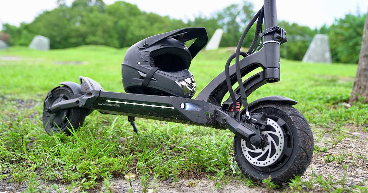 An electric scooter laid on its side on the grass, showcasing its robust frame and attached safety helmet, indicating preparation for the Electric Scooter Racing Series Championship with a focus on rider safety.