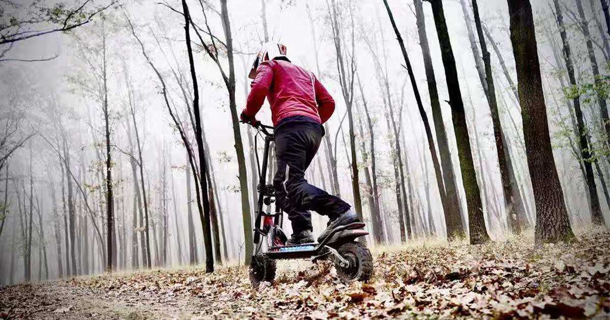 A racer clad in a red jacket and white helmet aggressively maneuvers an electric scooter through a misty, wooded trail, exemplifying the intensity of the Electric Scooter Racing Series Championship.