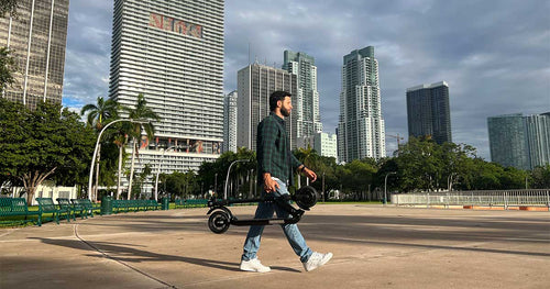 a man walking in a park with a portable electric scooter