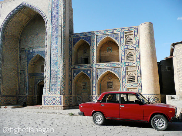 Red Lada parked in front of historic building in Bukhara, Uzbekistan.