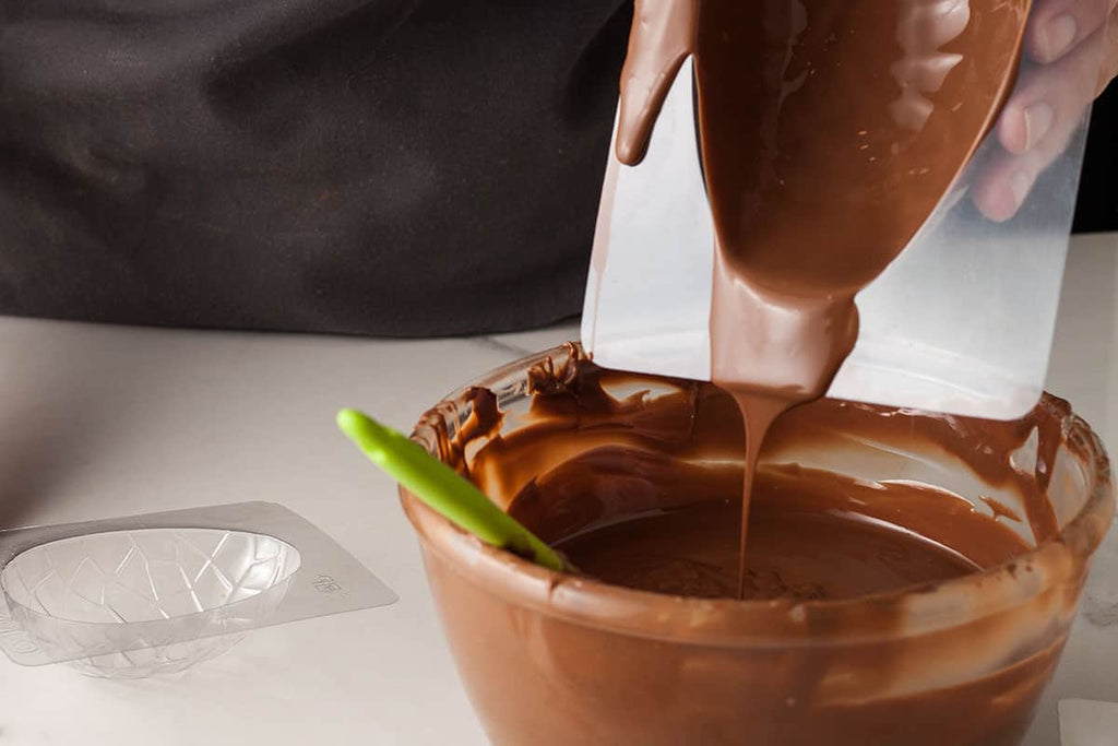 Easter egg mold filled with chocolate held over bowl of melted chocolate to pour off excess.