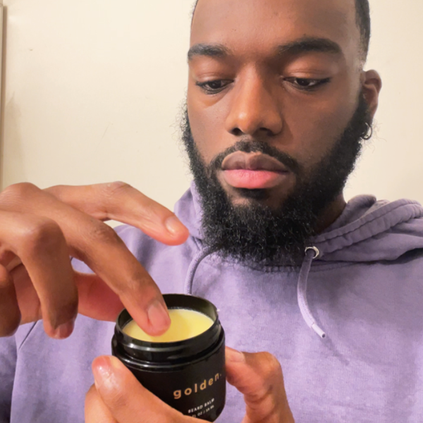 A black man applying beard balm on his wavy beard