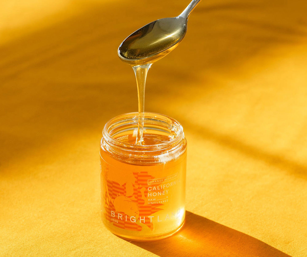 a spoon drizzling honey back into a jar of brightland california honey