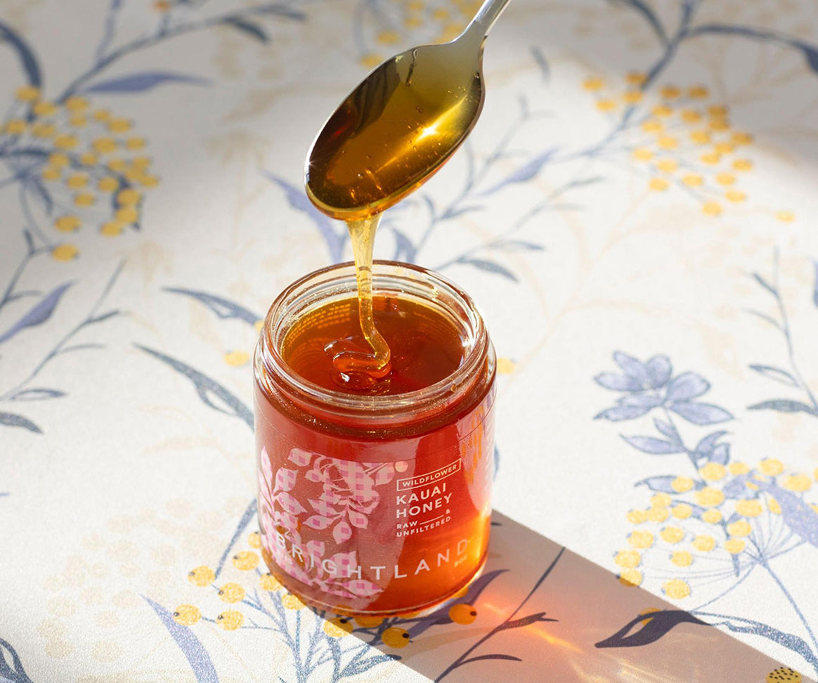 a spoon drizzling honey back  into a jar of brightland kauai honey