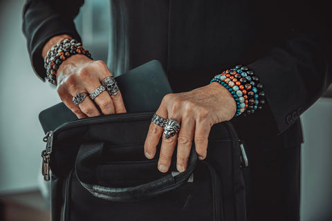 Man holding computer bag wearing silver rings and gemstone bracelets.