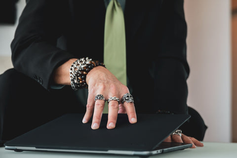 Man holding computer wearing bracelets and rings