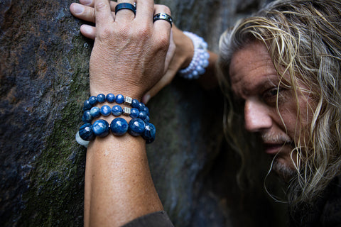 Male wearing Kyanite Gemstone Bracelets leaning against a stone wall.
