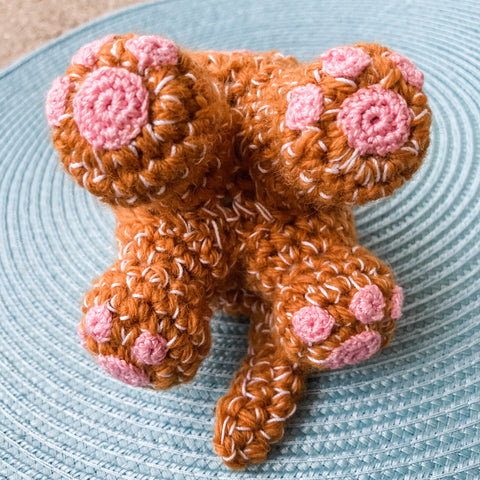 Crocheted orange cat on it's back so that the 4 feet bottoms are visible. Each foot has 4 toe beans. 