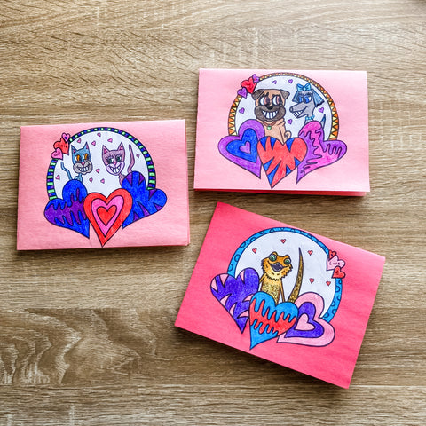 photo of 3 handmade Valentine's day featuring featuring a bearded dragon, cats in love, and dogs in love. There are patterned hears and geometric shapes.