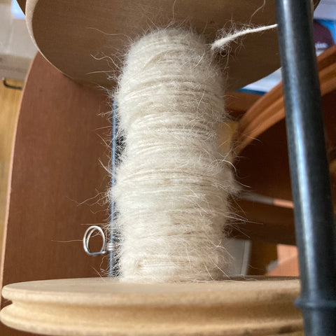 photo of a wooden bobbin on a spinning wheel with plyed dog fur handspun yarn