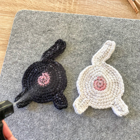 a black and a white cat butt crocheted coaster being sprayed by water out of a spray bottle