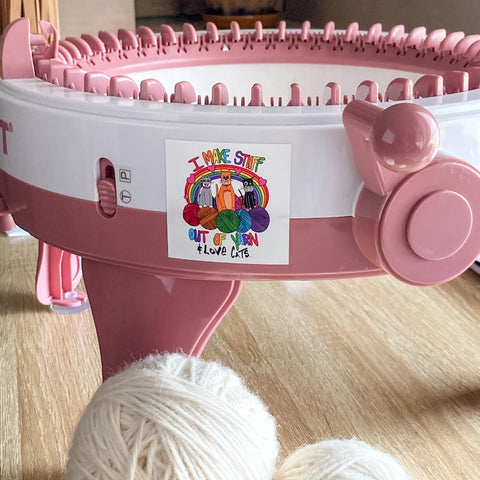 Colorful I make stuff out of yarn and love cats square sticker on a pink and white knitting machine with white balls of yarn in front 