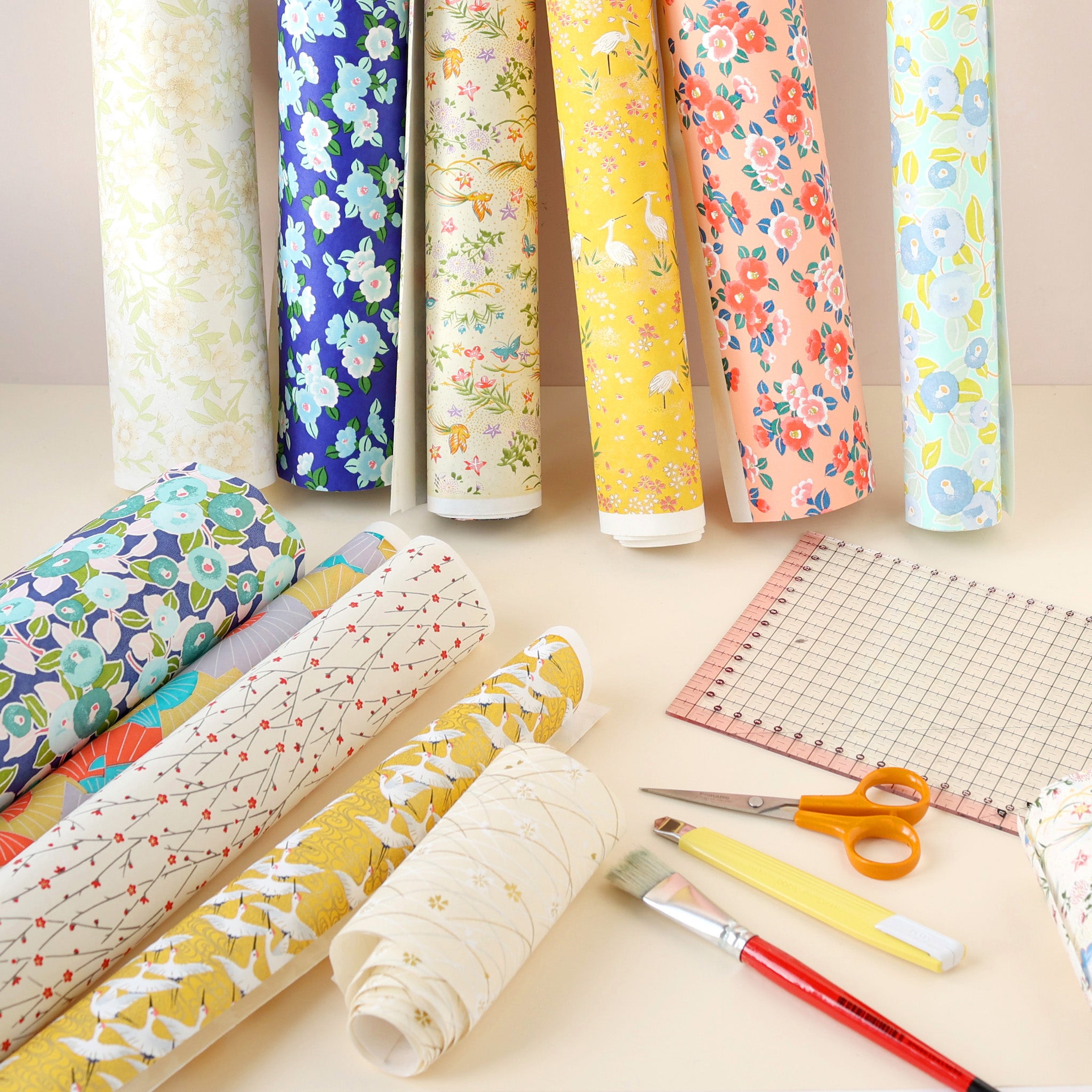rouleaux de papiers japonais aux couleurs et motifs variés et règle, pinceau, cutter et ciseaux