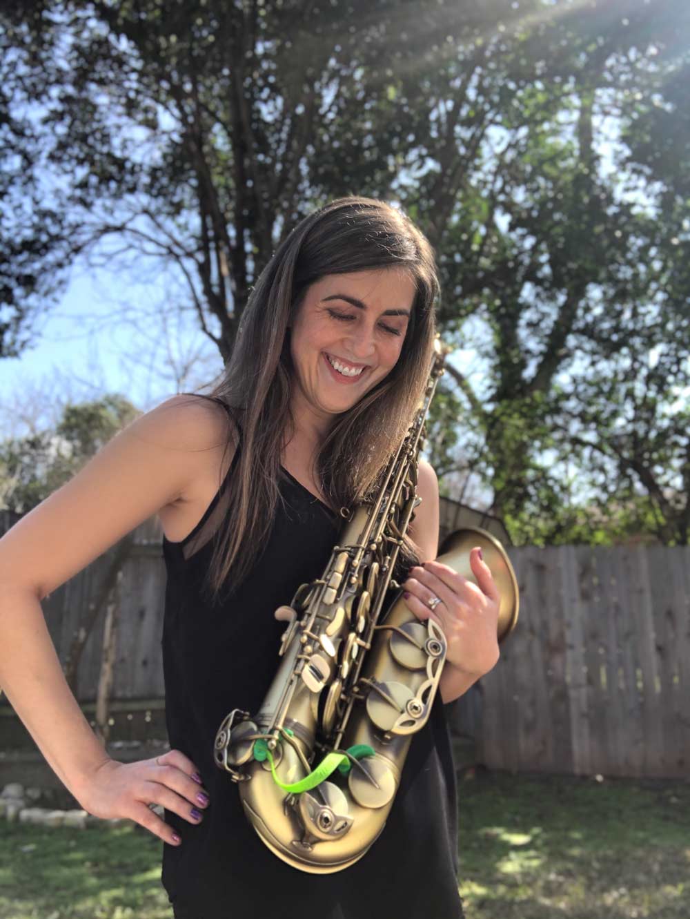 Saxophone player Elizabeth Rosinbum holding a tenor saxophone with green Key Leaves sax key props on it.