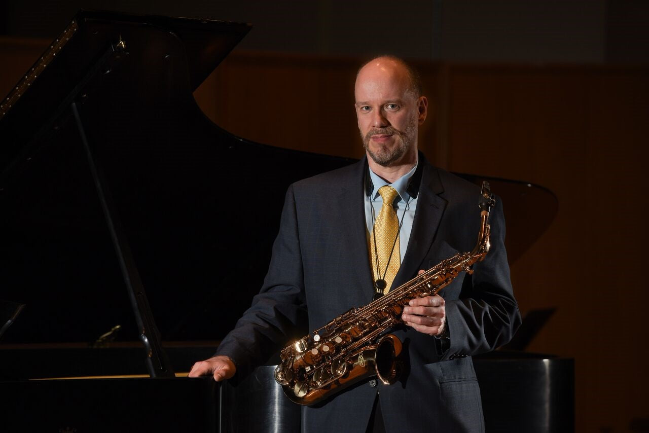 Greg Banaszak holding alto sax by piano